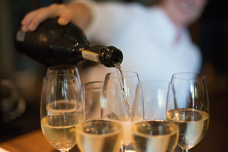 A person in a white shirt pours wine into a group of glasses in the foreground.