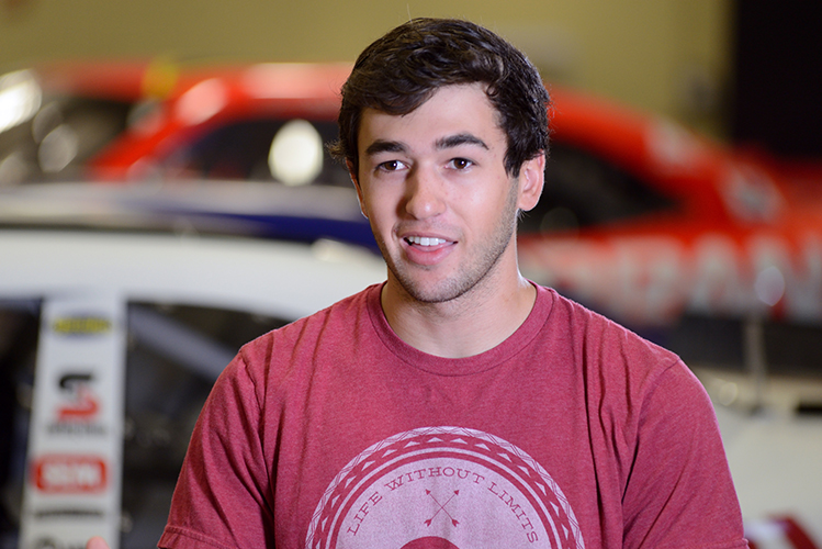 Portrait of a young man with racecars out of focus in the background.