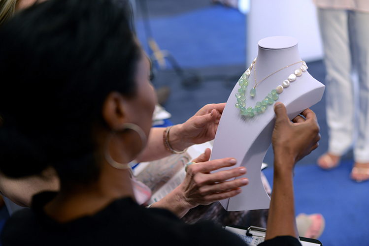 Over the shoulder photo of judges from a designer competition examine a necklace on a white display form.
