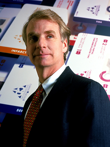 A man in a suit and patterned tie stands in front of a display featuring various key cards. He looks upward with a contemplative gaze.