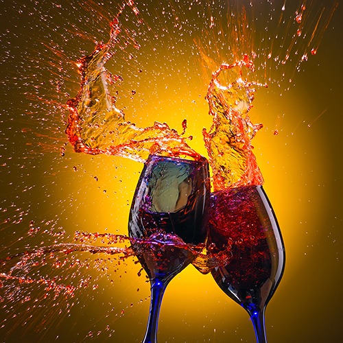 Two glasses of red wine collide against a vibrant yellow background, creating a splash of wine that captures a dynamic and celebratory moment.