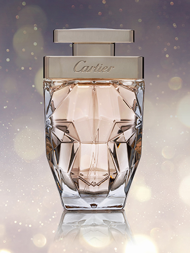 A luxurious perfume bottle with a faceted, diamond-like design and the word Cartier on the cap. The background is a soft, glowing bokeh effect with warm tones, emphasizing the elegance and sophistication of the fragrance.