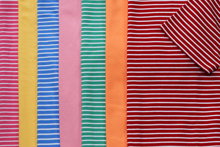 Several colorful striped fabrics are arranged side by side. From left to right, they are pink, yellow, blue, pink, green, orange, with a red and white striped fabric overlapping on the right.