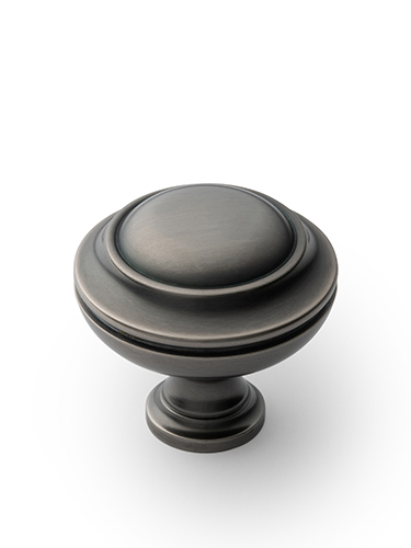 A metallic, round cabinet knob with a brushed finish, featuring circular ridges on the top. It has a classic and elegant design, resting on a short, cylindrical stem, against a white background.