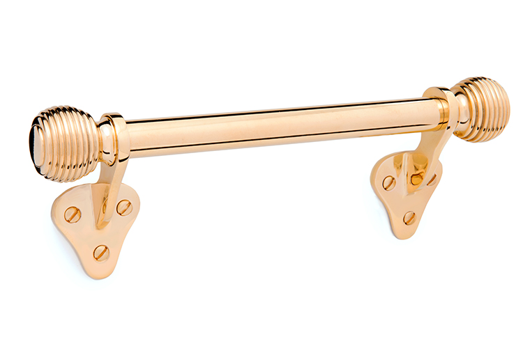 A decorative polished brass window handle with ribbed cylindrical ends, mounted on two triangular brackets with three screw holes attached to a plain white surface.